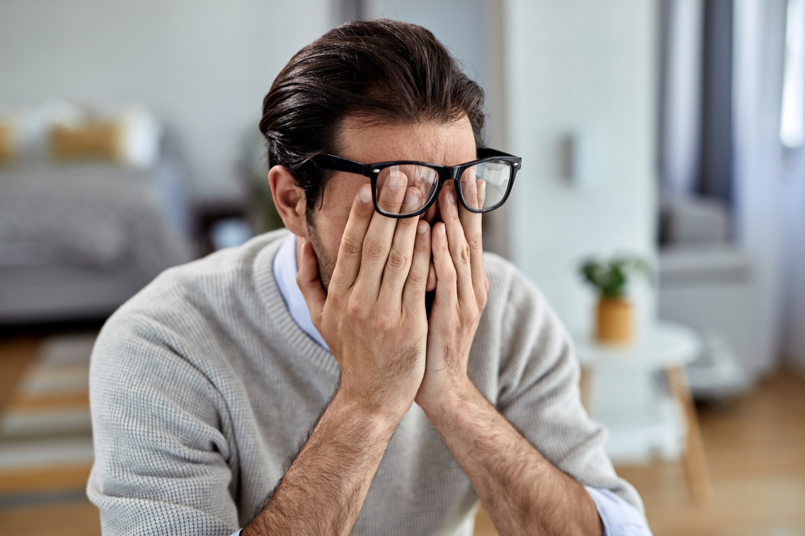 A tired man rubbing his eyes at home